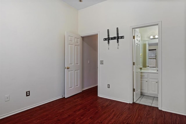 unfurnished bedroom featuring ensuite bath, baseboards, and wood finished floors