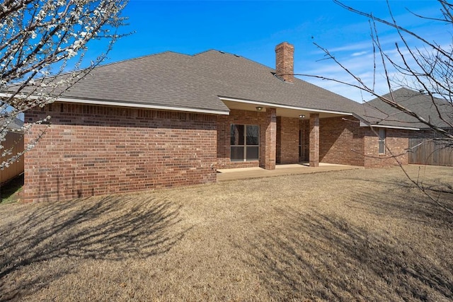 back of house featuring a patio, a chimney, brick siding, and a shingled roof