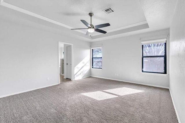 carpeted empty room with visible vents, baseboards, a tray ceiling, and a ceiling fan