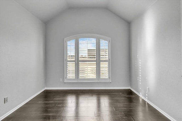 spare room with baseboards, dark wood-style floors, and vaulted ceiling