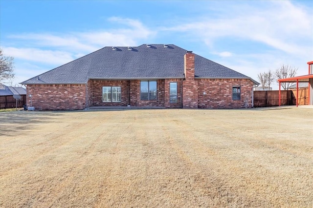 back of house with brick siding, a lawn, a chimney, and fence