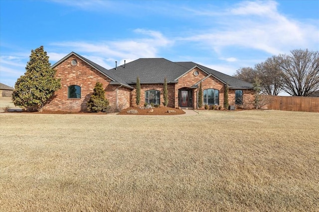 view of front facade featuring a front yard, fence, brick siding, and a shingled roof