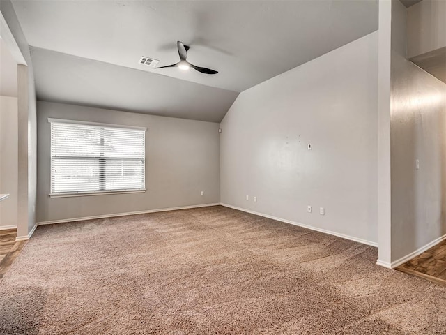 carpeted empty room with visible vents, baseboards, ceiling fan, and vaulted ceiling