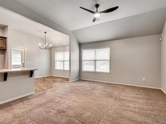 unfurnished living room with light carpet, ceiling fan with notable chandelier, baseboards, and lofted ceiling