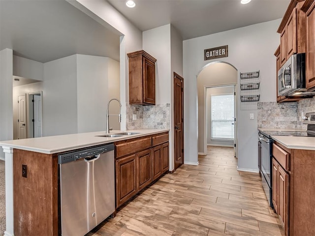 kitchen featuring a peninsula, arched walkways, a sink, appliances with stainless steel finishes, and brown cabinets