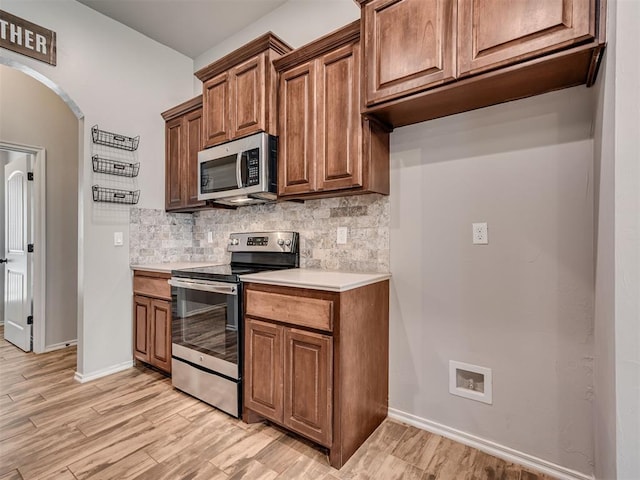 kitchen featuring arched walkways, light countertops, appliances with stainless steel finishes, light wood-type flooring, and backsplash