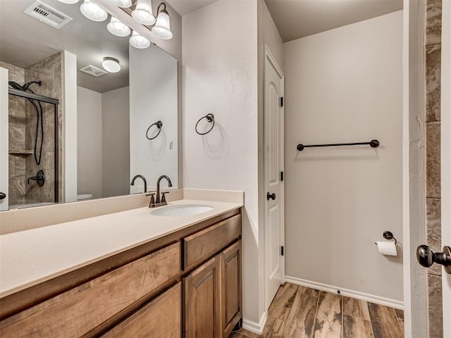 bathroom featuring visible vents, baseboards, a tile shower, wood finished floors, and vanity