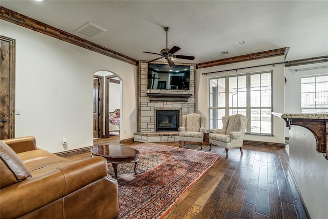 living area featuring visible vents, dark wood-type flooring, ornamental molding, a fireplace, and arched walkways