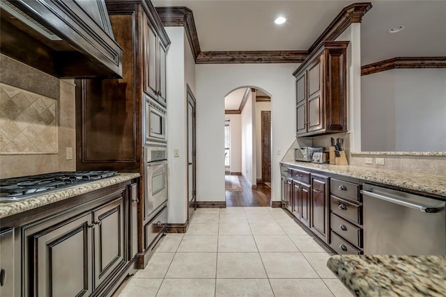 kitchen featuring premium range hood, ornamental molding, stainless steel appliances, arched walkways, and light tile patterned flooring