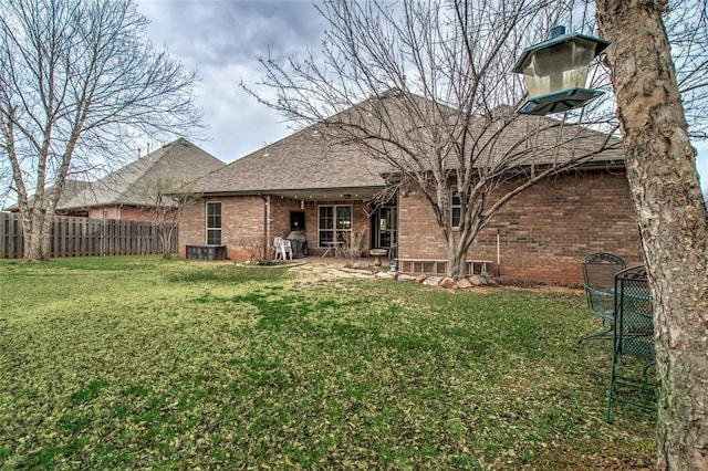 back of property with brick siding, a shingled roof, a yard, and fence