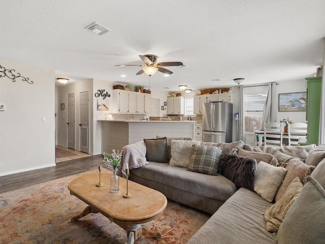 living area with visible vents, baseboards, ceiling fan, light wood-type flooring, and a textured ceiling