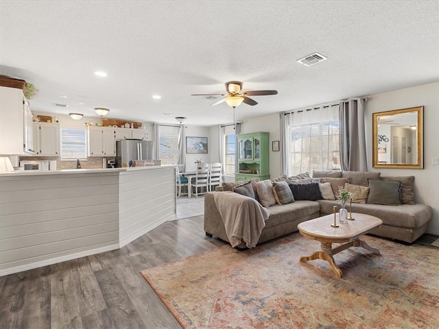 living area with visible vents, a textured ceiling, wood finished floors, and a ceiling fan