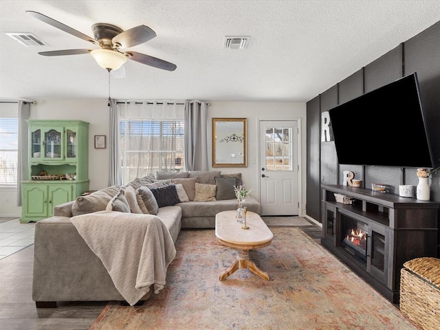 living room featuring visible vents, ceiling fan, a textured ceiling, and a lit fireplace