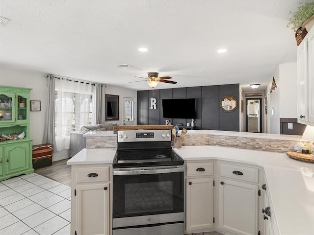 kitchen featuring open floor plan, a peninsula, stainless steel electric range, white cabinets, and light countertops