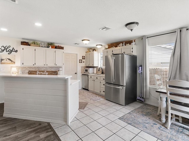 kitchen with visible vents, a peninsula, a sink, stainless steel appliances, and light countertops