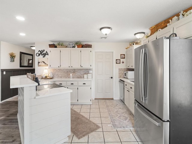 kitchen with light countertops, light tile patterned floors, a peninsula, stainless steel appliances, and white cabinetry