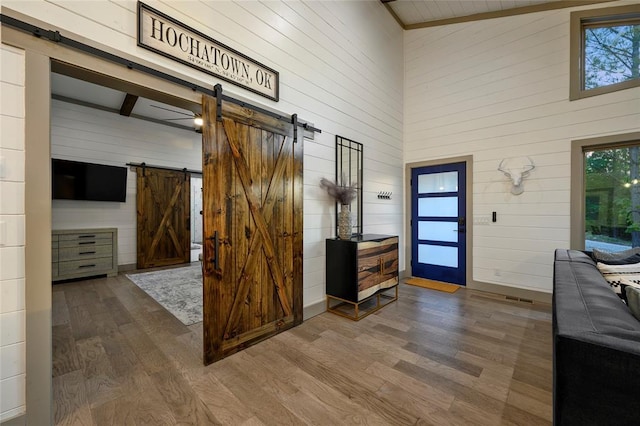 entrance foyer featuring wooden walls, visible vents, a barn door, a high ceiling, and wood finished floors