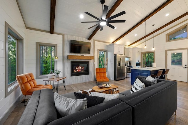 living room featuring vaulted ceiling with beams, a large fireplace, light wood-style floors, and a ceiling fan