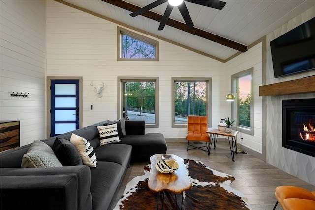 living area featuring a glass covered fireplace, beam ceiling, wood finished floors, and ceiling fan