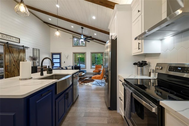 kitchen featuring blue cabinetry, wall chimney range hood, beamed ceiling, stainless steel appliances, and a sink