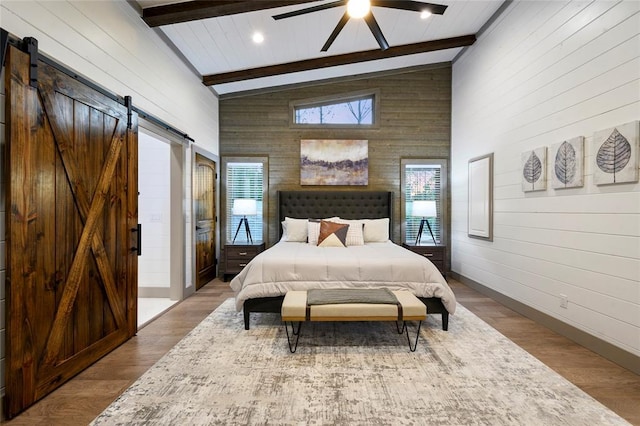 bedroom with beam ceiling, high vaulted ceiling, a barn door, and wood finished floors