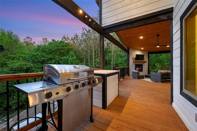 patio terrace at dusk with a deck, area for grilling, a warm lit fireplace, and grilling area