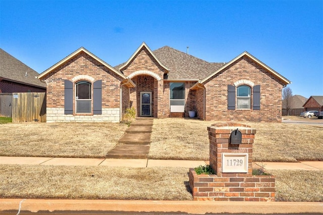 view of front of property featuring fence, brick siding, and a shingled roof