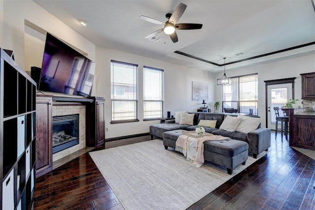 living area featuring a ceiling fan, visible vents, dark wood finished floors, a tray ceiling, and a fireplace