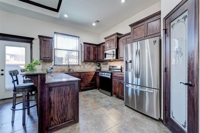 kitchen with tasteful backsplash, a peninsula, stone countertops, stainless steel appliances, and a sink