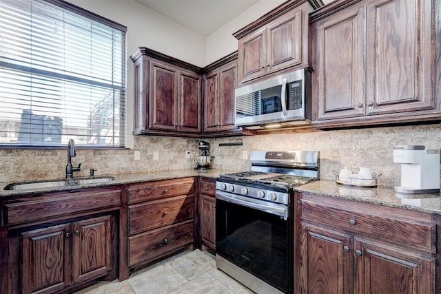 kitchen featuring backsplash, light stone counters, light tile patterned floors, appliances with stainless steel finishes, and a sink