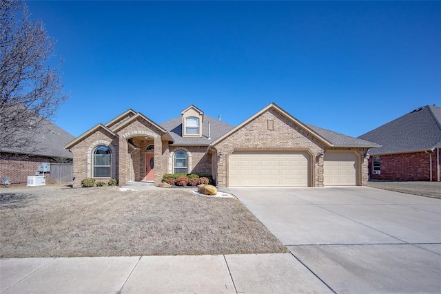 french country home with a garage, brick siding, and driveway