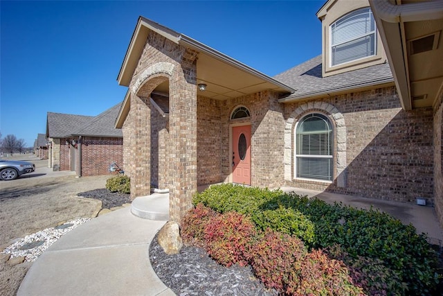 entrance to property featuring brick siding and roof with shingles