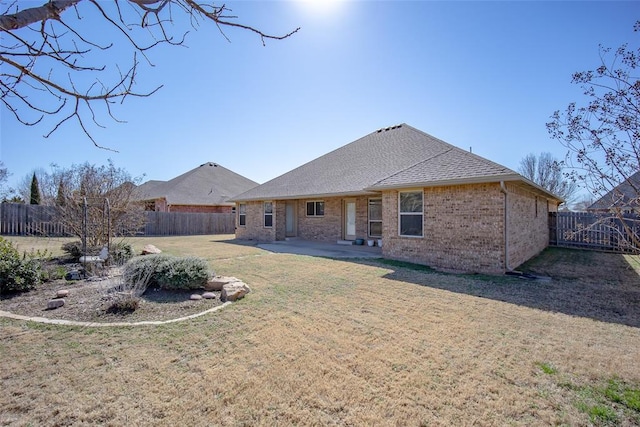 rear view of house with a fenced backyard, a yard, a shingled roof, brick siding, and a patio area