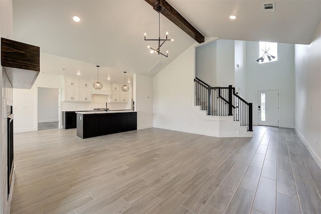8101 Jenny Ln, Edmond, OK 73034 - unfurnished living room featuring a chandelier, beam ceiling, stairway, light wood-type flooring, and high vaulted ceiling