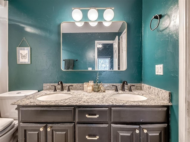 bathroom featuring double vanity, toilet, a textured wall, and a sink