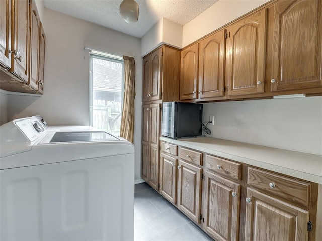 washroom with cabinet space, light tile patterned floors, washer and dryer, and a textured ceiling