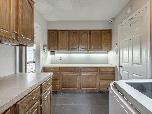 kitchen with brown cabinets, a textured ceiling, light countertops, and dark tile patterned flooring