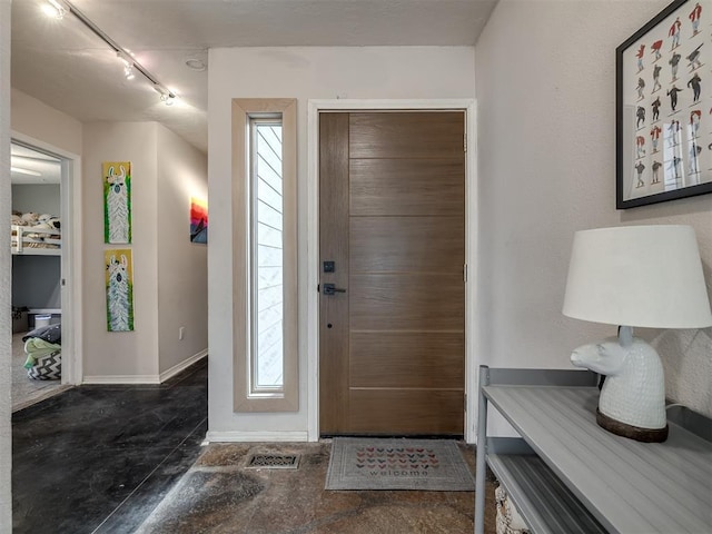 foyer with rail lighting, concrete flooring, and baseboards