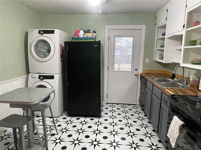 kitchen featuring light floors, open shelves, a sink, black appliances, and stacked washer and clothes dryer