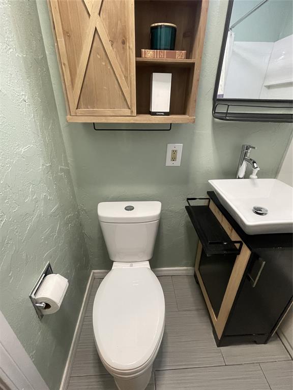 bathroom featuring toilet, vanity, baseboards, and a textured wall