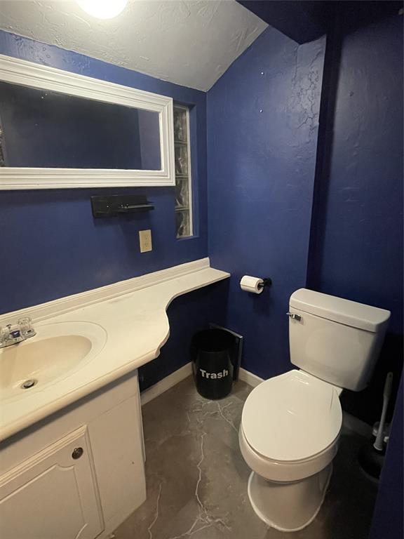 half bathroom featuring vanity, baseboards, lofted ceiling, a textured ceiling, and toilet