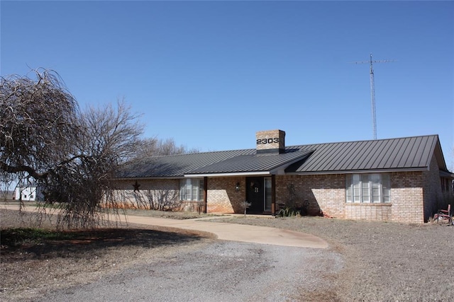 view of front facade featuring brick siding, a chimney, metal roof, and a standing seam roof