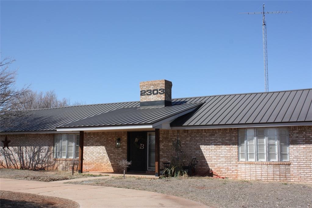 view of front of property featuring metal roof, brick siding, a chimney, and a standing seam roof