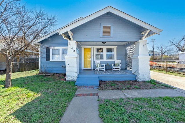 bungalow-style home featuring a porch, a front lawn, and fence