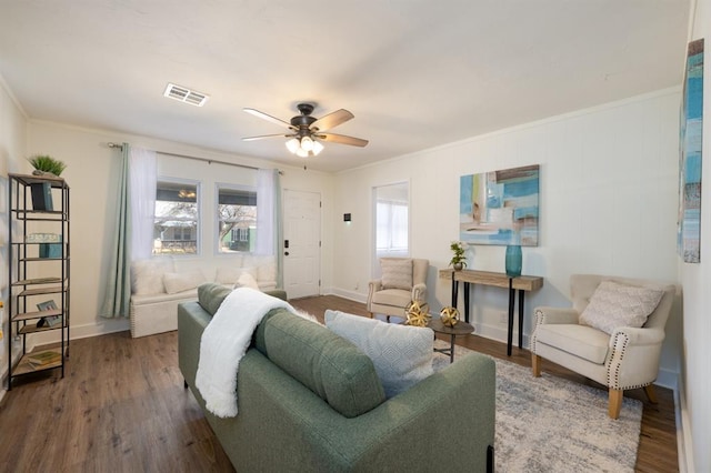 living area with visible vents, baseboards, ornamental molding, wood finished floors, and a ceiling fan