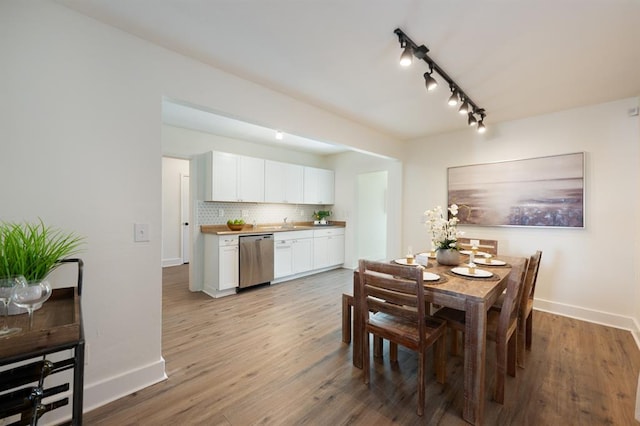 dining space with baseboards, track lighting, and light wood finished floors