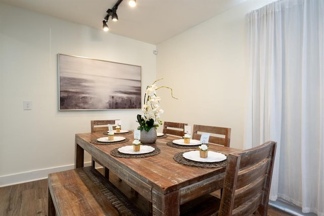 dining space featuring rail lighting, baseboards, and wood finished floors