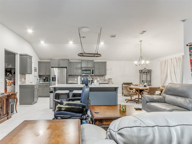 living area featuring an inviting chandelier, visible vents, and vaulted ceiling