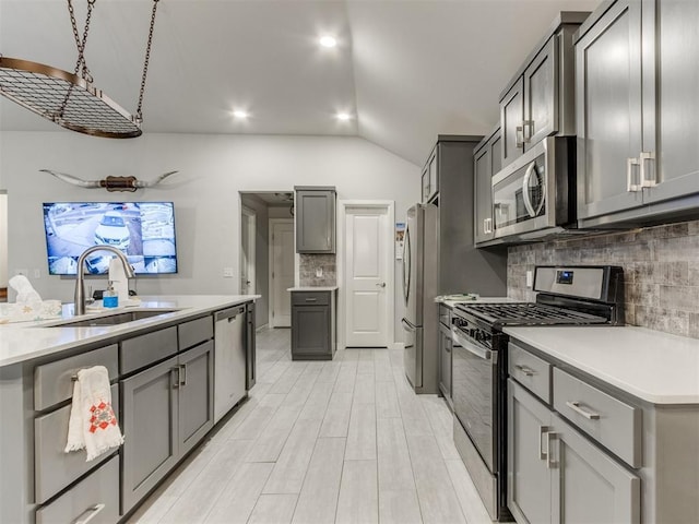 kitchen featuring light countertops, vaulted ceiling, gray cabinets, appliances with stainless steel finishes, and a sink