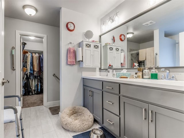 bathroom with visible vents, double vanity, a sink, a shower stall, and a spacious closet